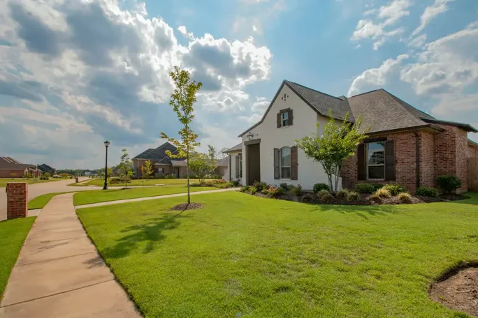 Suburban brick house with a manicured lawn under a bright sky.