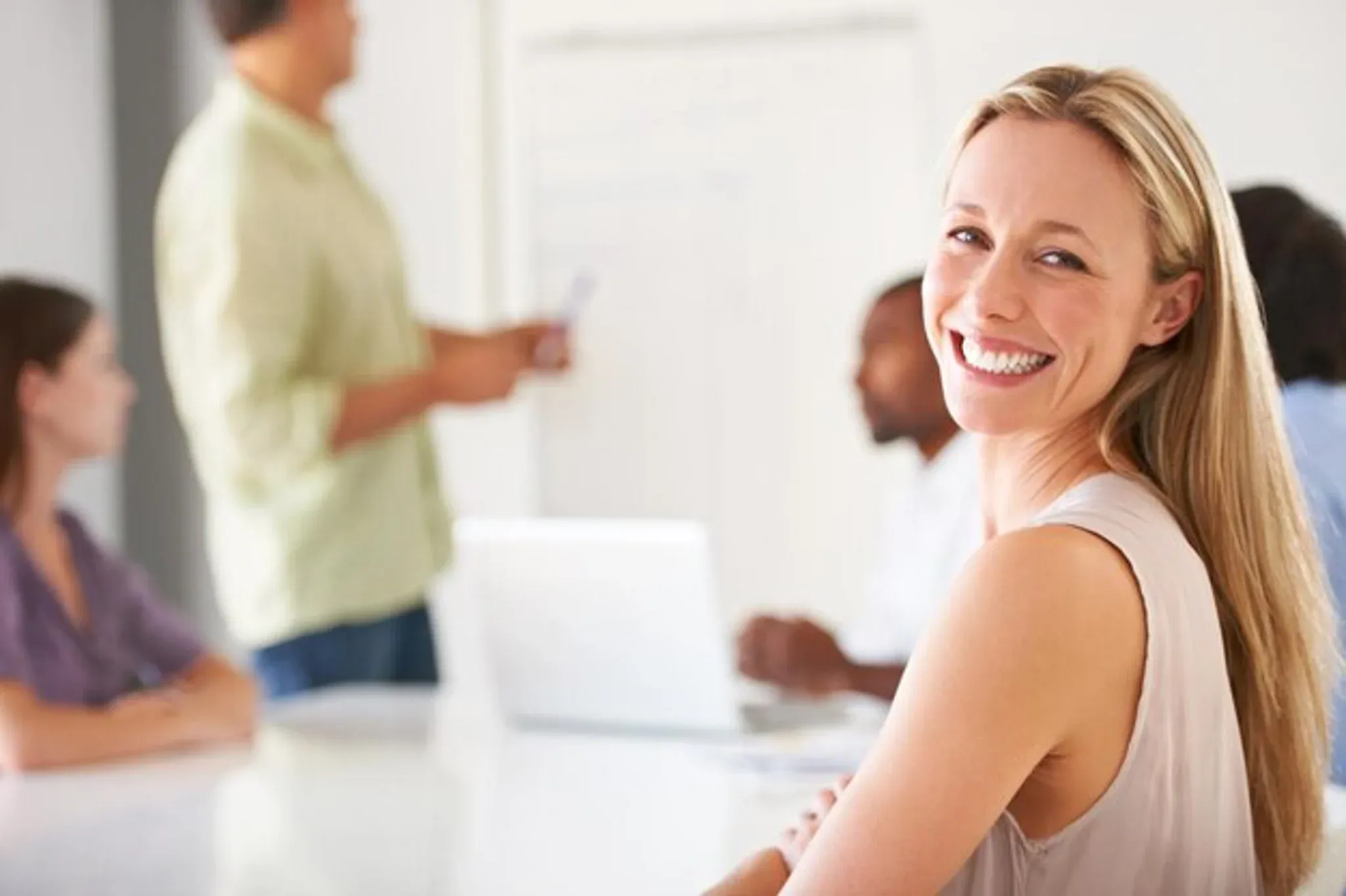 Woman smiling in a meeting while colleagues collaborate in the background.